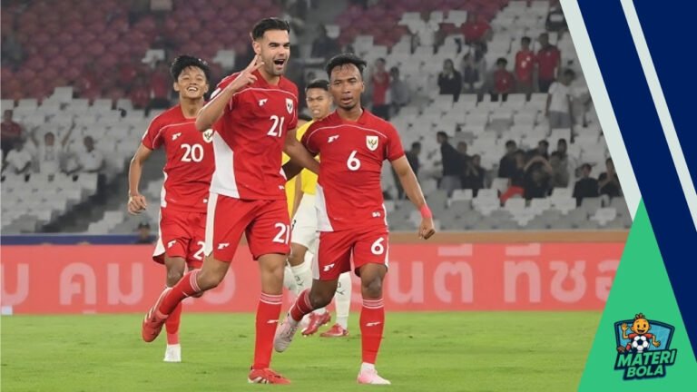 Empat pemain sepak bola berbaju merah berada di lapangan, salah satu dari mereka mengacungkan simbol damai. Latar belakang menunjukkan stadion dengan penonton.